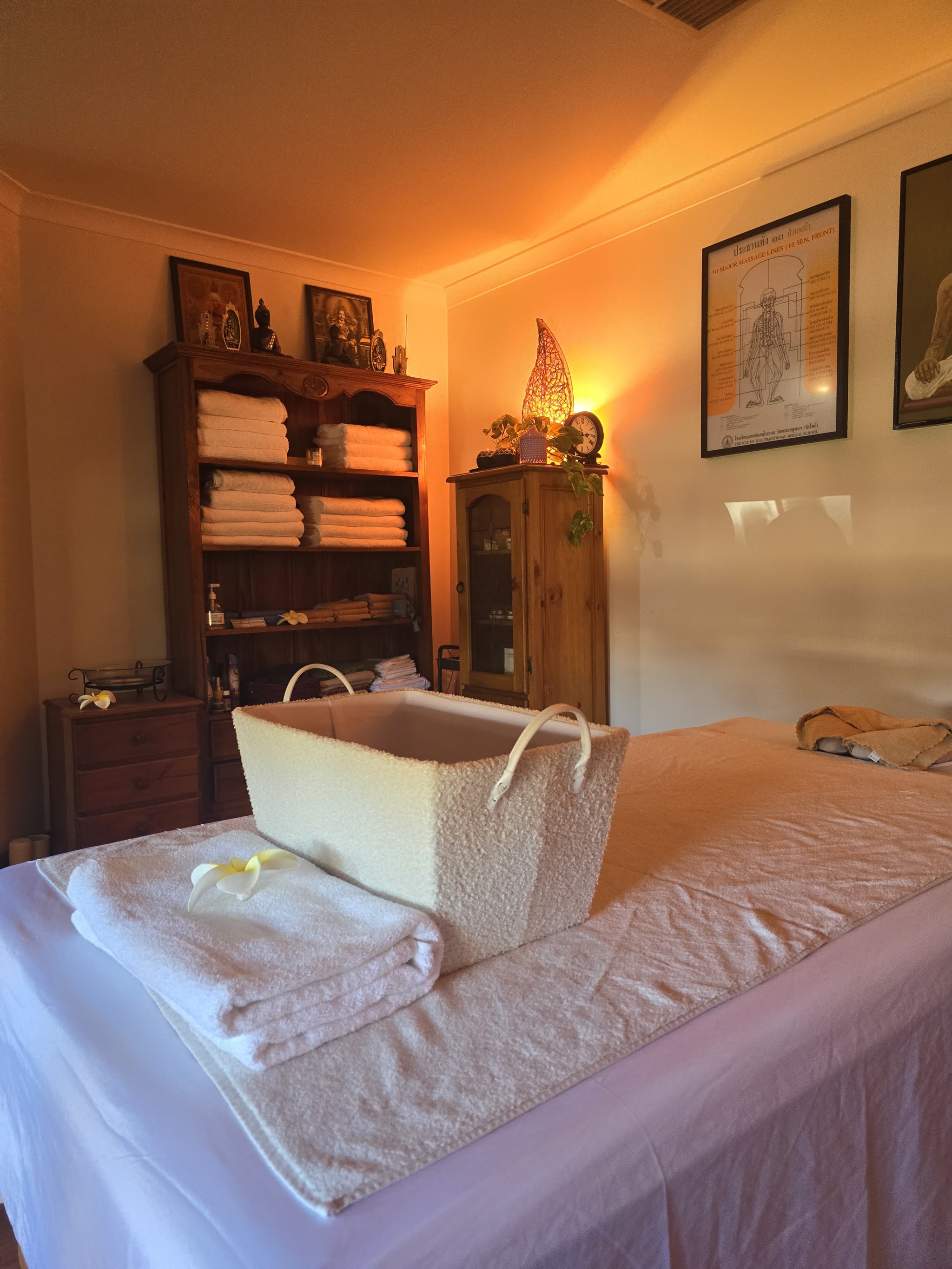 A corner of the treatment room with shelves of towels, a framed Thai massage chart and the table made up for the next client
